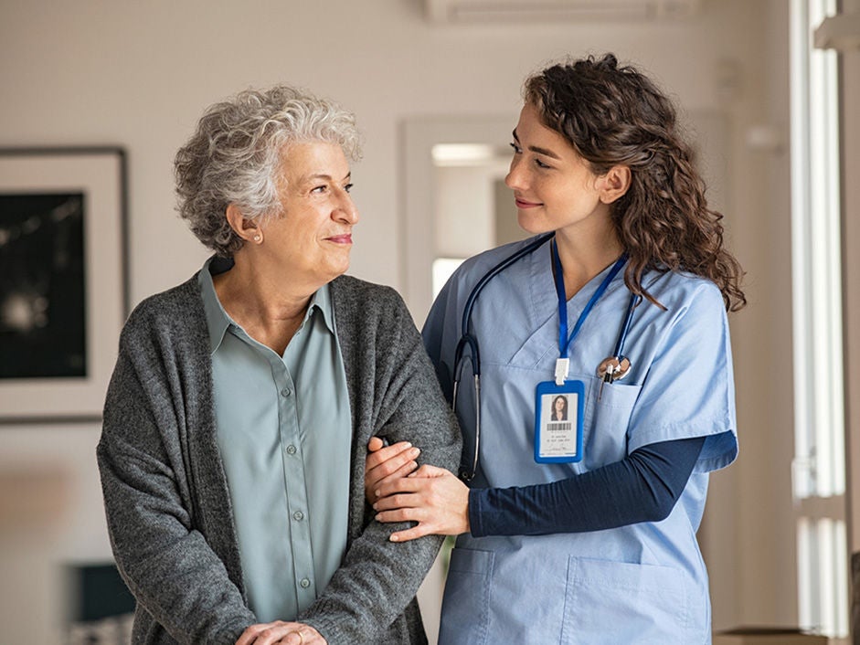 Health care provider holding onto the arm of a standing older woman.