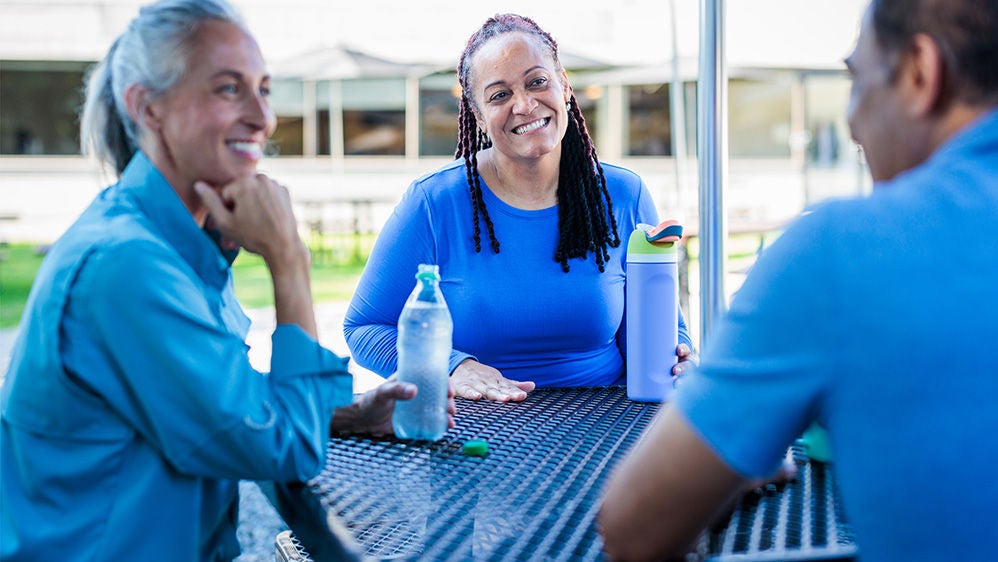 Two smiling women and a man sitting at a table otuside..