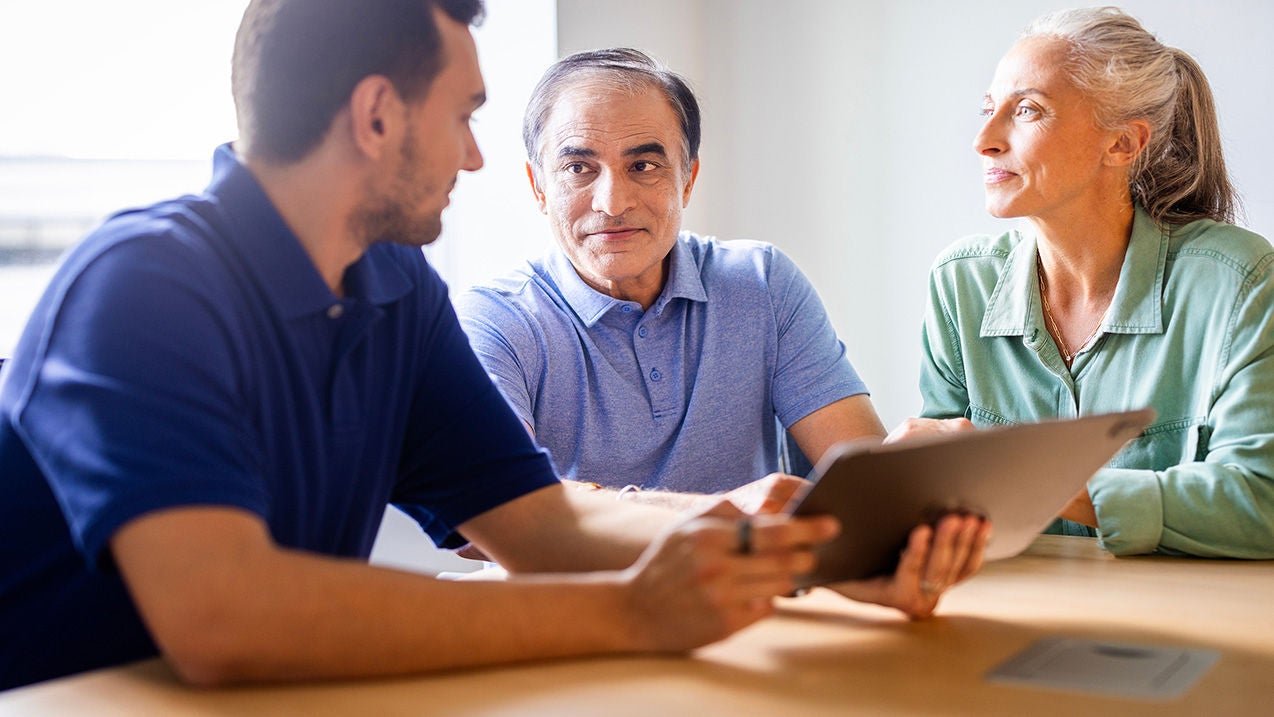 older couple sitting with young man looking at tablet together.