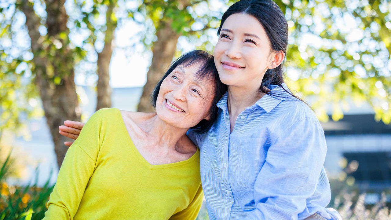 women sitting outside leaning into each other and smiling.