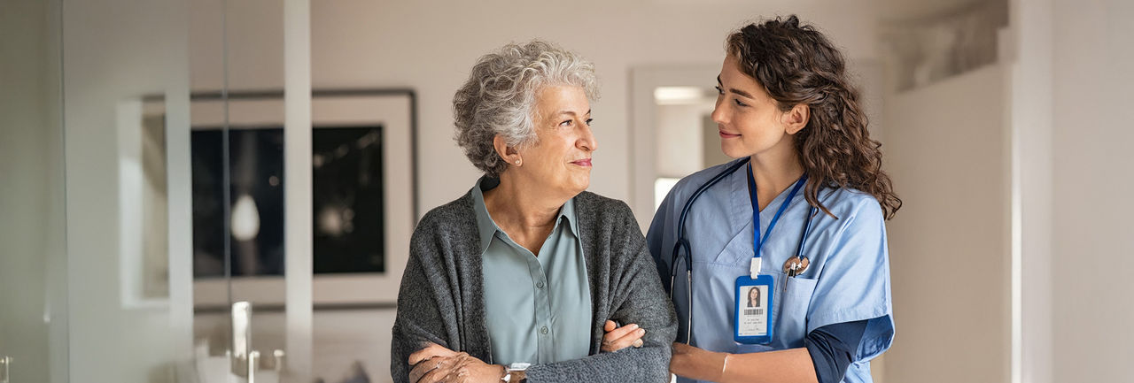 Female health care provider walking with an older woman.