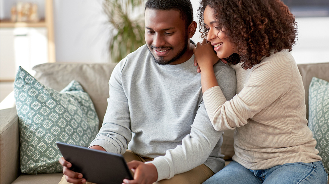 Smiling couple sitting on a sofa looking at a tablet.