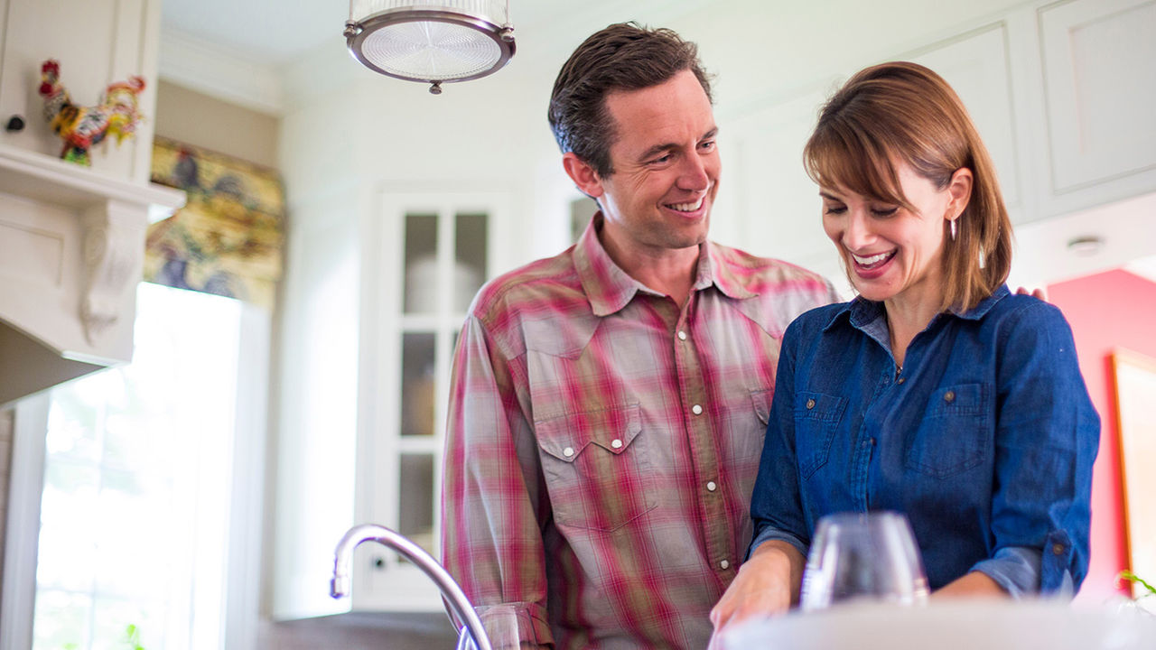 Happy couple standing in a kitchen at the sink.