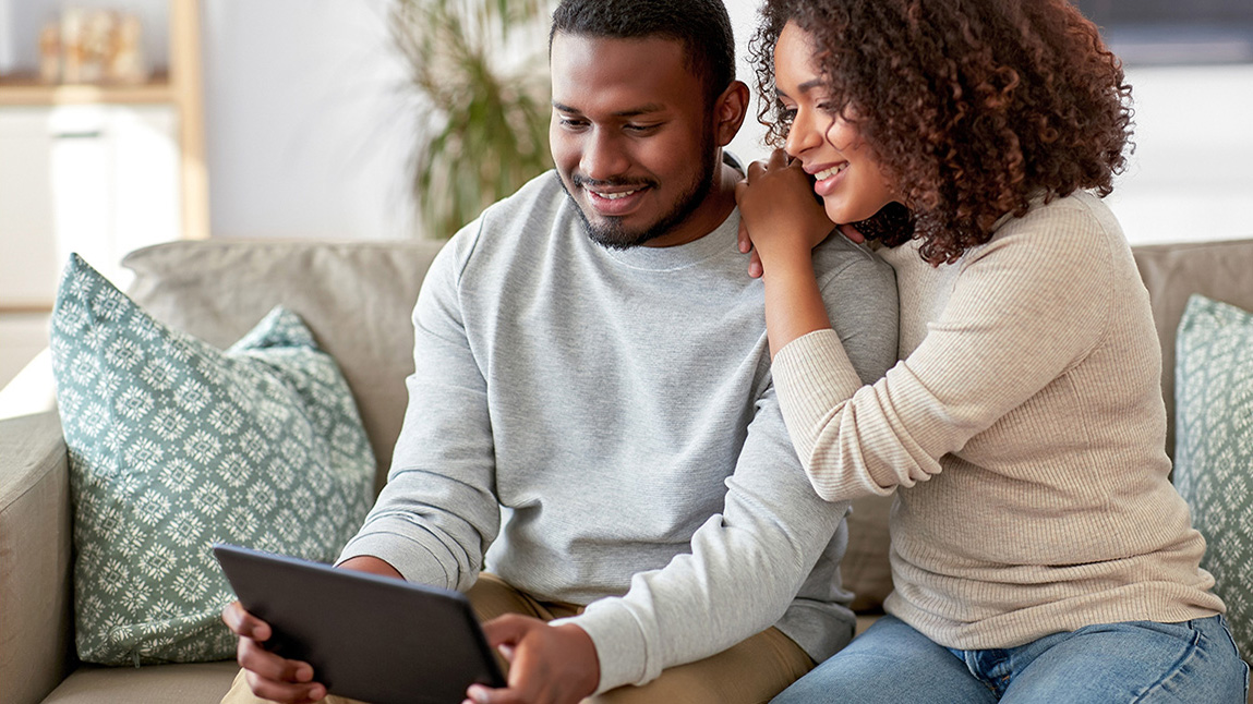 couple sitting on couch smiling and looking at ipad